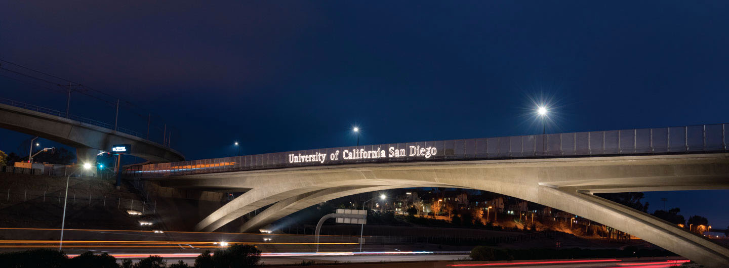 Bridge-overpass over the I-5, lit up at night with the UC San Diego logo